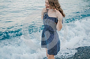 Romantic traveler woman in a blue dress walks on waves along the Mediterranean coast. The girl runs barefoot on the