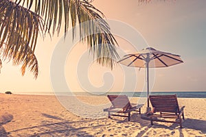 Romantic tropical sunset scenic, two sun beds, loungers, umbrella under palm tree leaves. White sand landscape sea view horizon