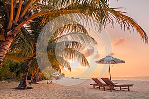 Romantic tropical sunset scenic, two sun beds, loungers, umbrella under palm tree leaves. White sand landscape sea view horizon