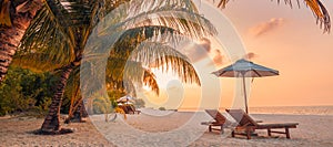 Romantic tropical sunset scenic, two sun beds, loungers, umbrella under palm tree leaves. White sand sea panorama landscape