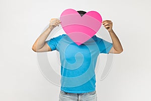 Romantic unknown anonymous man holding big pink heart in front his face expressing fondness and love photo