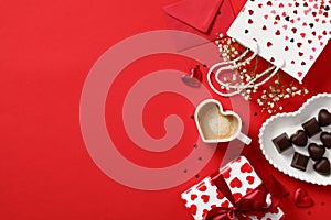 Romantic Valentine`s Day concept. Top view Love letter, heart-shaped coffee cup, candies, and gift box on red background