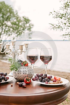 Romantic Valentine`s day dinner on the beach: two glasses of red wine, fresh fruit and a candlestick