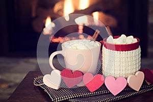 Romantic Valentine`s Day Fireplace Scene with Red and Pink Cocoa Mugs and Wood Hearts Garland in Cozy Setting with room or space f