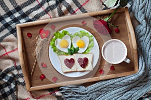 Romantic valentines day breakfast in bed with heart-shaped eggs, toasts, jam, coffee, rose and petals