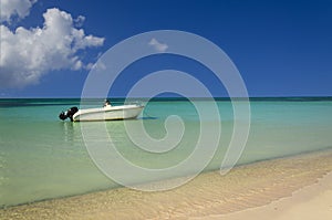 Romantic view of white boat on azure ocean against perfect blue sky and gold sand beach.