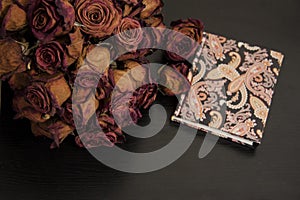 Romantic vintage composition on dark background. Red dry rose flowers and notebook.