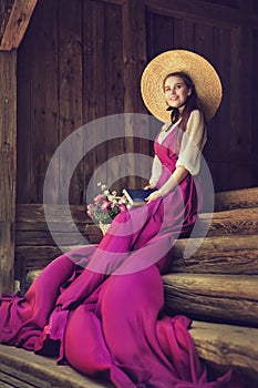 Romantic Vintage Woman in Summer Hat dreaming with Book on wooden Stairs Background. Victorian Fashion Portrait
