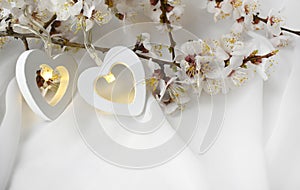 Romantic wedding composition with flowering almond branch, couple of heart lights on white silk background. Elegant greeting conce