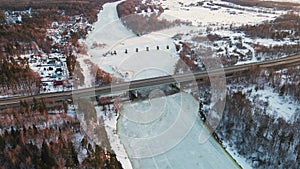 Romantic winter landscape with frozen river and bridge at sunset, aerial view.