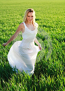 Romantic woman in dress running across green field