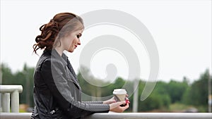 Romantic woman in a leather jacket and with a coffee in her hands looks away