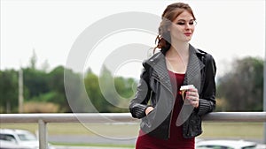 Romantic woman in a leather jacket and with a coffee in her hands looks away