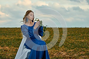 Romantic woman portrait. female in blue dress holds white rose in her hands while sitting on chair in the field