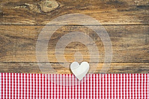 Romantic wooden love heart on red checkered fabric and rustic wood background.