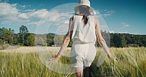 Romantic young adult woman walk on agricultural meadow and touch harvest