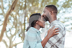 Romantic young African man kissing his girlfriend`s forehead outdoors