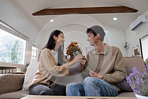 Romantic young asian couple embracing with holding flowers and smiling in living room at home. fall in love. Valentine