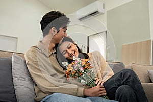 Romantic young asian couple embracing with holding flowers and smiling in living room at home. fall in love. Valentine