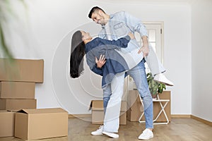 Romantic young couple dancing in room with cardboard boxes on moving day
