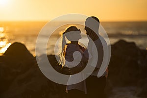 A romantic young couple date by the ocean during a lovely sunset.