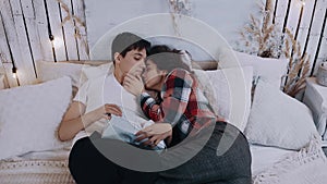 Romantic young couple embracing while sitting on the bed in the bedroom on Christmas Eve.