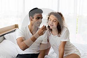 Romantic young couple enjoying cake together on the bed in bedroom