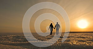 Romantic young couple holding hands and walking on the beach as the sun begins to set.