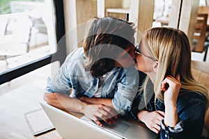 Romantic young couple kissing while sitting at cafe and using la