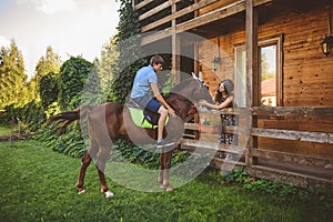 Romantic young couple in love, a walk on a horse on nature background and wooden country-style hotel. A man sits astride