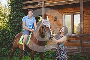 Romantic young couple in love, a walk on a horse on nature background and wooden country-style hotel. A man sits astride
