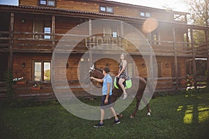 Romantic young couple in love, a walk on a horse on nature background and wooden country-style hotel. Young woman