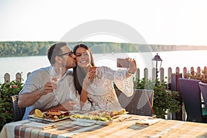 Romantic young couple posing for a selfie, eating dinner in a riverside restaurant