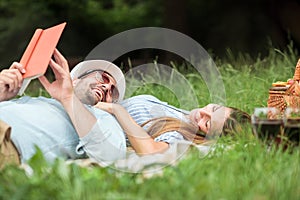 Romantic young couple relaxing in a park, lying on a picnic blanket, reading books