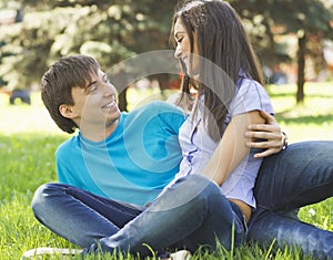 Romantic young couple sitting together at park on the grass and