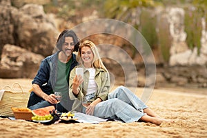 Romantic young couple taking selfie while having picnic at the beach