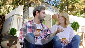 Romantic young couple. travel trailer background, drinking wine in nature, chatting, having fun. Boyfriend and