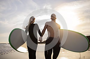 Romantic Young Couple Walking With Surfboards On Sunset Beach And Holding Hands