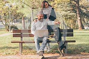 Romantic young happy couple in love enjoying their time and playing with little black dog in sunny autumn garden