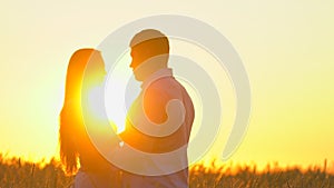 Romantic young happy couple silhouette in golden wheat field at sunset. Woman and man hugging and kissing against