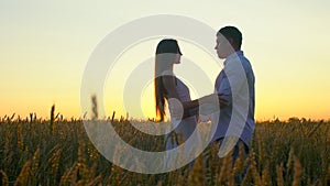 Romantic young happy couple silhouette in golden wheat field at sunset. Woman and man hugging and kissing against