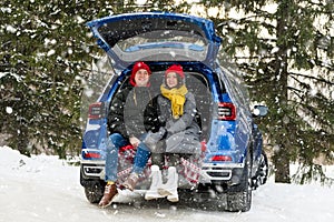 Romantic young hipster couple hugging while sitting in car trunk under falling snow. Love, valentines and holiday