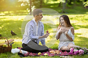 Romantic young man making proposal to his surprised girlfriend on picnic at park