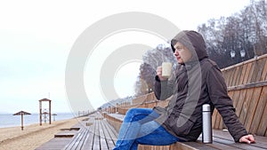 Romantic young man relaxing on the beach with , drinking hot tea or coffee from thermos. Calm and cozy evening.