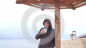 Romantic young man relaxing on the beach with , drinking hot tea or coffee from thermos. Calm and cozy evening.