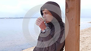 Romantic young man relaxing on the beach with , drinking hot tea or coffee from thermos. Calm and cozy evening.