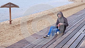 Romantic young man relaxing on the beach with , drinking hot tea or coffee from thermos. Calm and cozy evening.