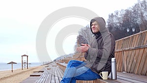 Romantic young man relaxing on the beach with , drinking hot tea or coffee from thermos. Calm and cozy evening.