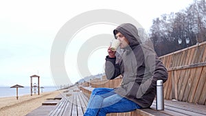 Romantic young man relaxing on the beach with , drinking hot tea or coffee from thermos. Calm and cozy evening.