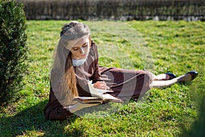 Romantic young woman reading a book in the garden sitting on the grass. Relax outdoor time concept.